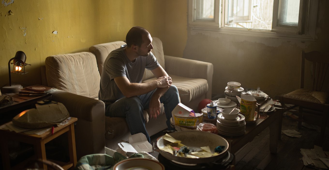 Мужчина сидит на диване в грязной комнате